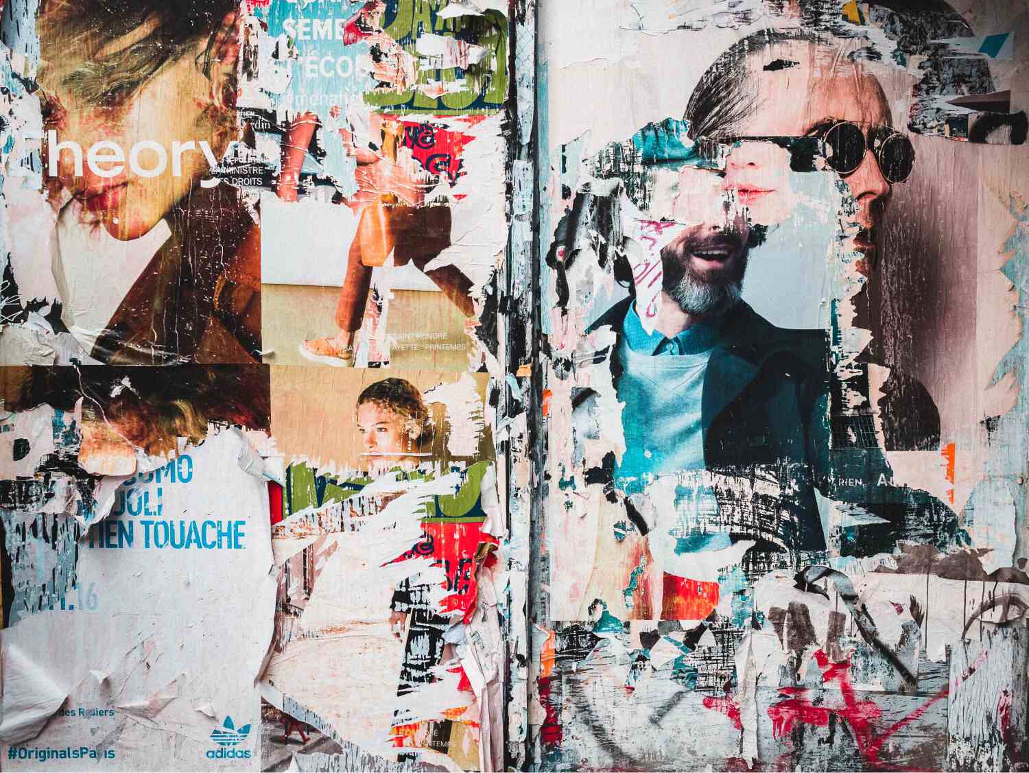 A colorful patchwork of old, partly-torn posters on a wall, with various words interspersed across incl. 'theory', 'touache' and 'Adidas' with the brand logo in the bottom left, and the faces of two men with beards, one with sunglasses, and two young women 